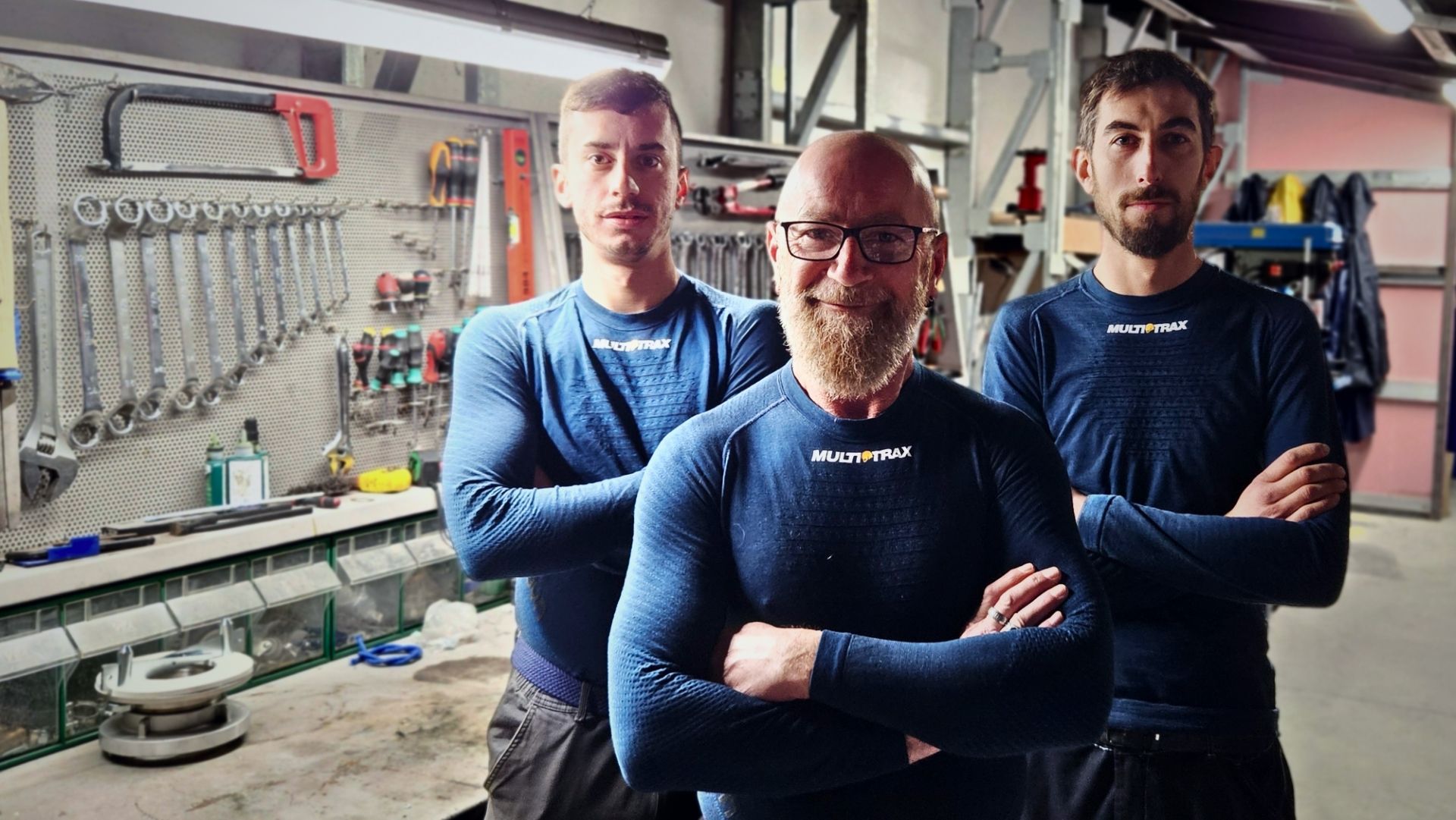 Tre impiegati di Multitrax, in posa davanti a un banco da lavoro, indossano le maglie della linea UYN for MULTITRAX