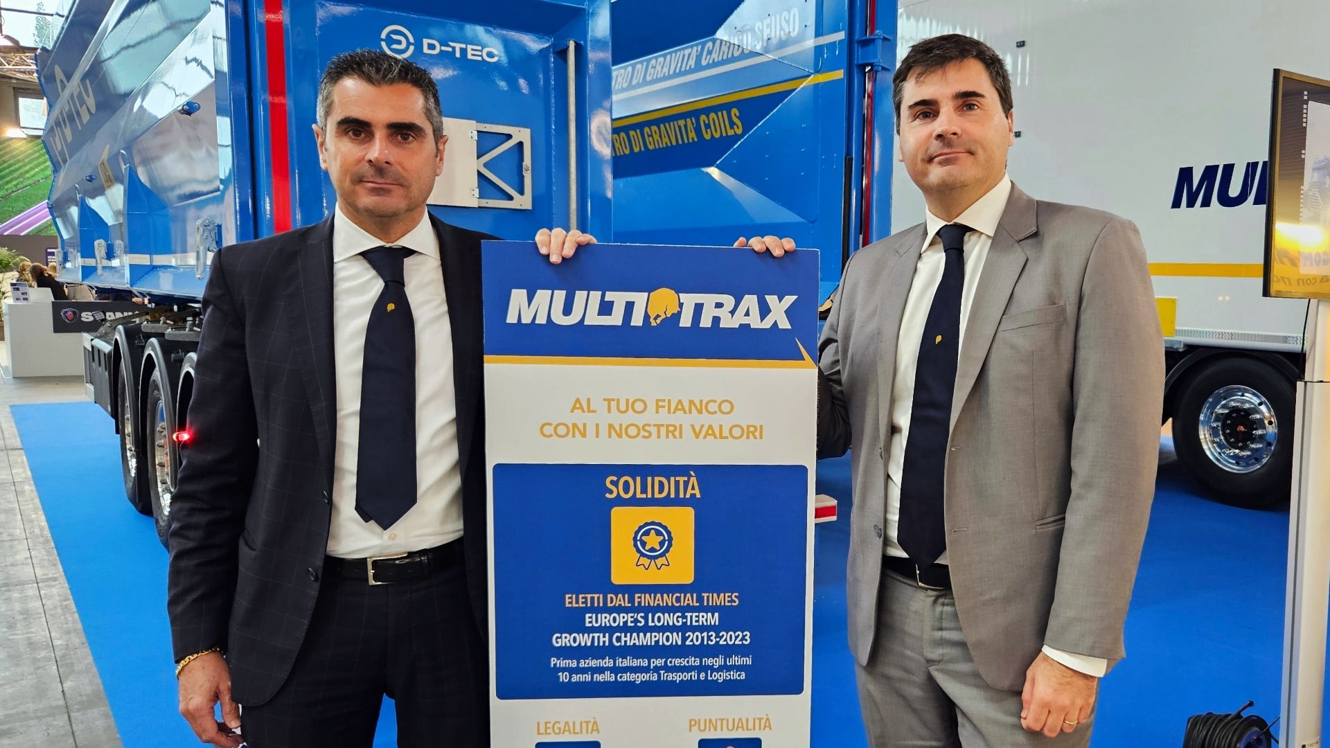 Andrea e Alberto Maggi intorno a un totem che illustra i principi di governance di Multitrax, davanti a un semirimorchio aperto